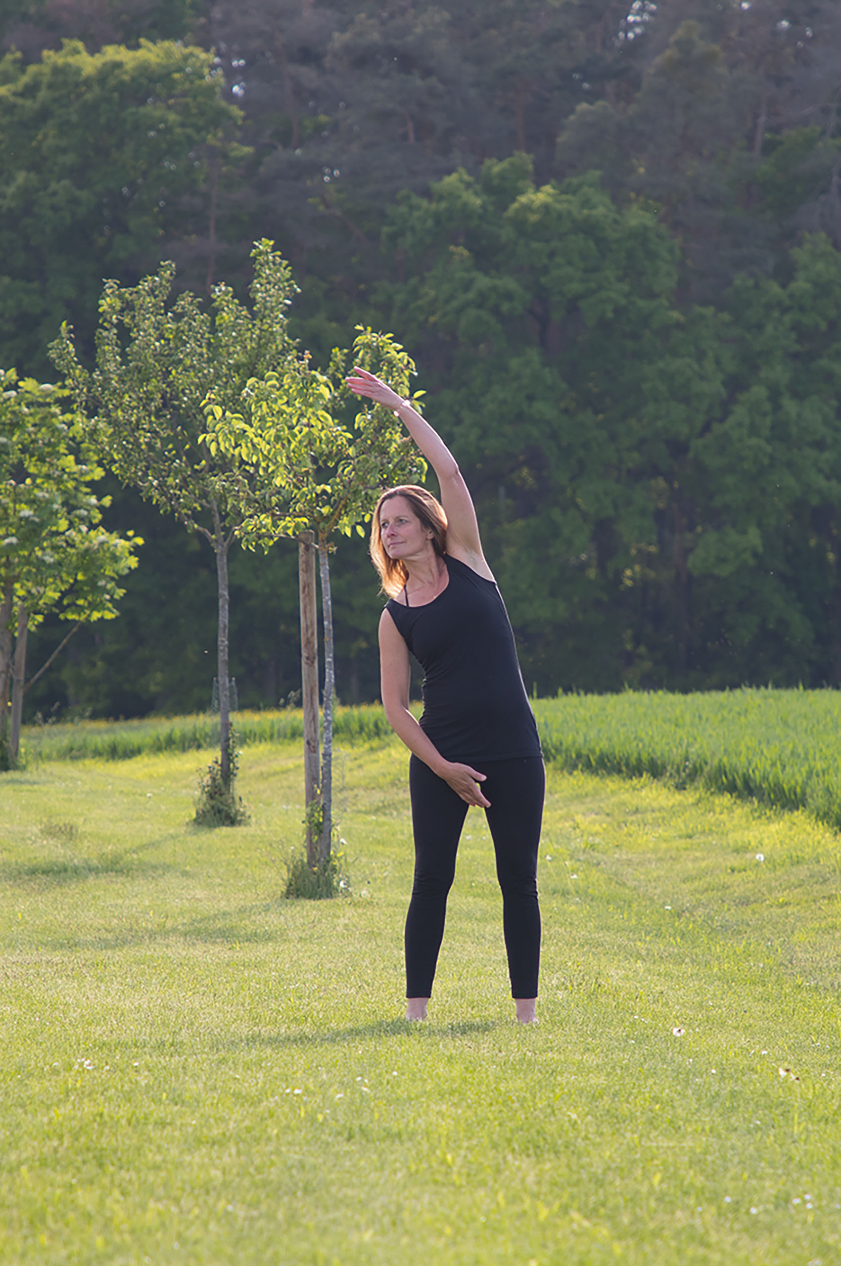 Eine Frau in stehender Yogastellung in einem Obstgarten