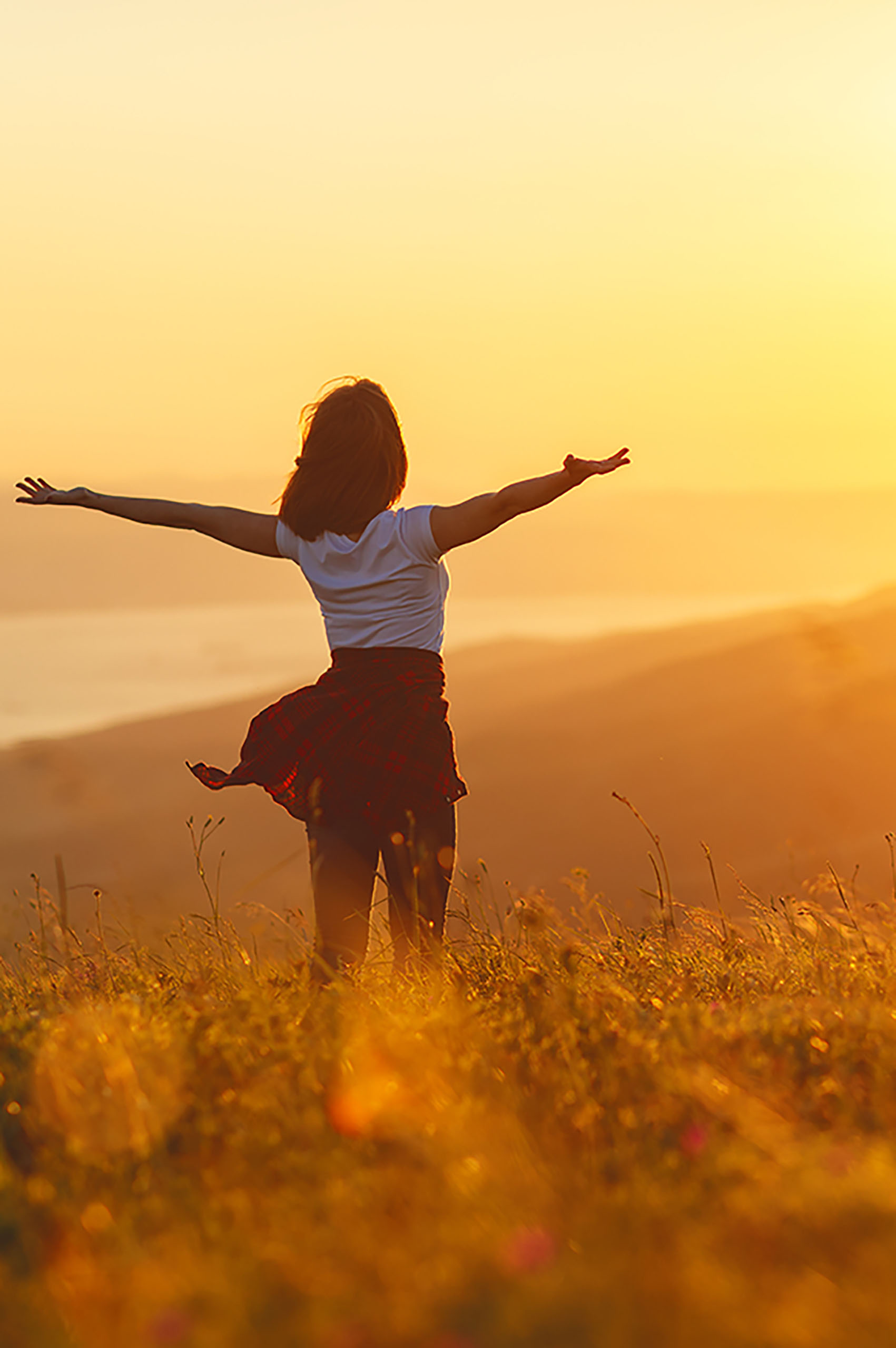 Frau_mit_ausgebreiteten_Armen_steht_in_Wiese_bei_Abendstimmung